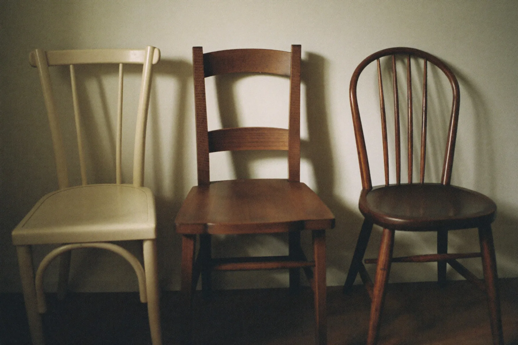 Drie verschillende stoelen naast elkaar tegen een muur.