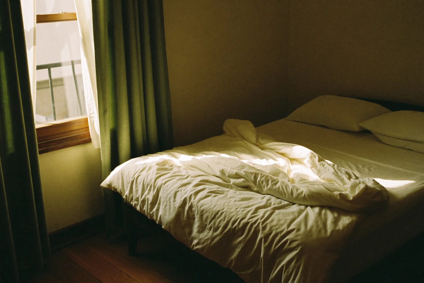 Een opgemaakt bed bij half open gordijnen, vroege zon over het beddengoed.