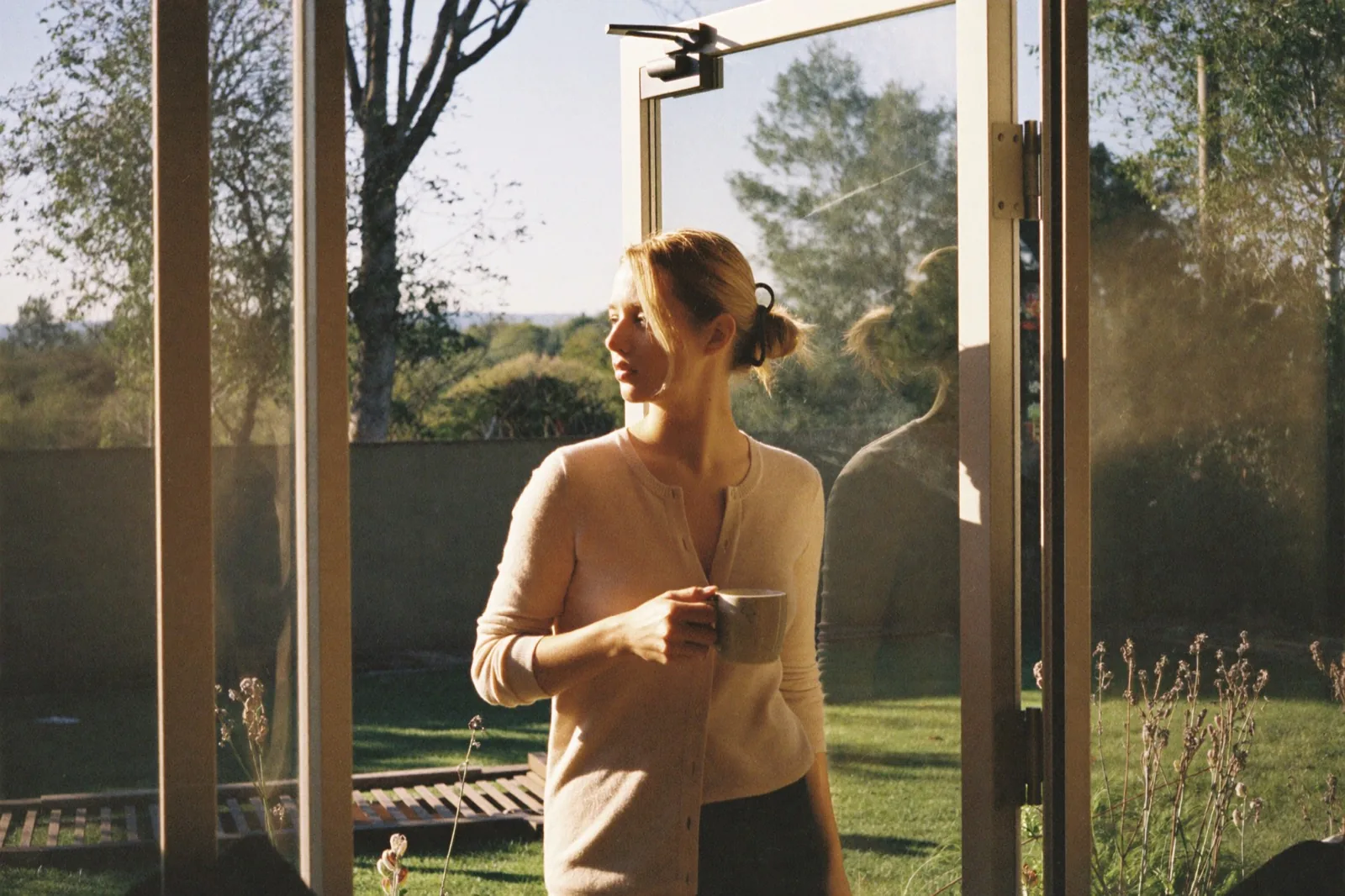 Een vrouw in de deuropening naar de tuin met een mok in beide handen