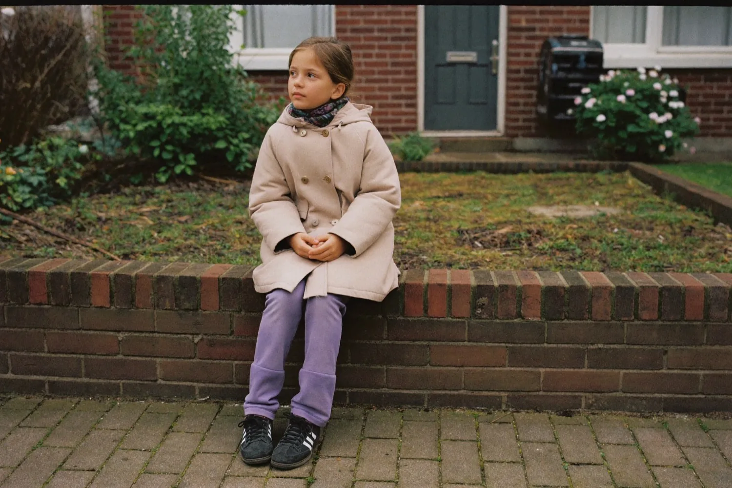 Een meisje van een jaar of negen alleen op een muurtje voor een rijtjeshuis