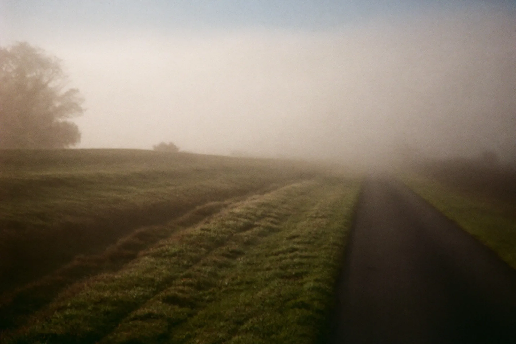 Mist boven een landweg: de richting zichtbaar, de details niet.