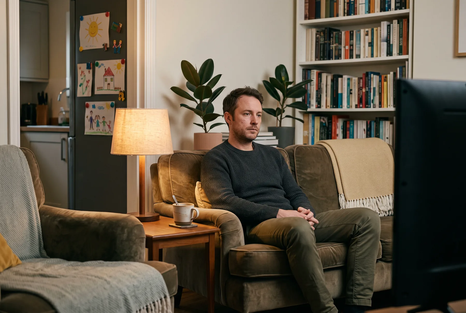 Een man alleen op de bank in een opgeruimde woonkamer, de televisie uit, koffie half op