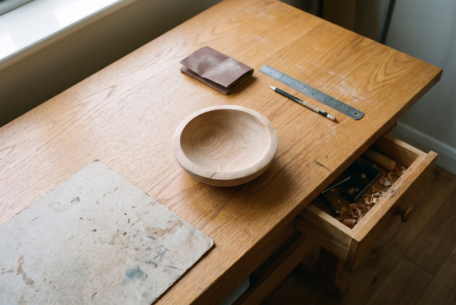 Een half afgeschuurde houten schaal op een werktafel, gereedschap overdreven netjes op een rij