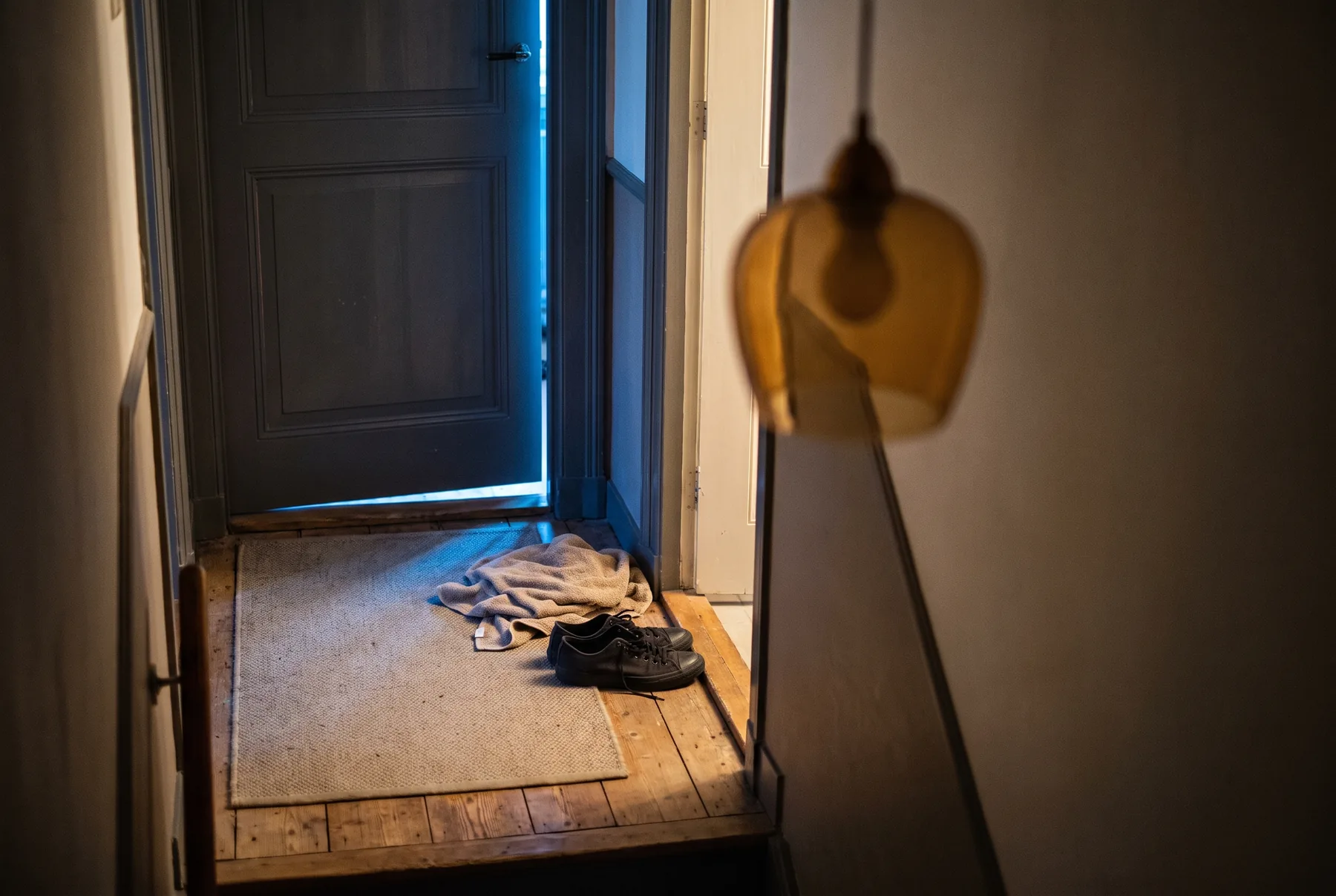Een gesloten slaapkamerdeur op een overloop in de nacht, met een streep koud blauw licht eronderdoor