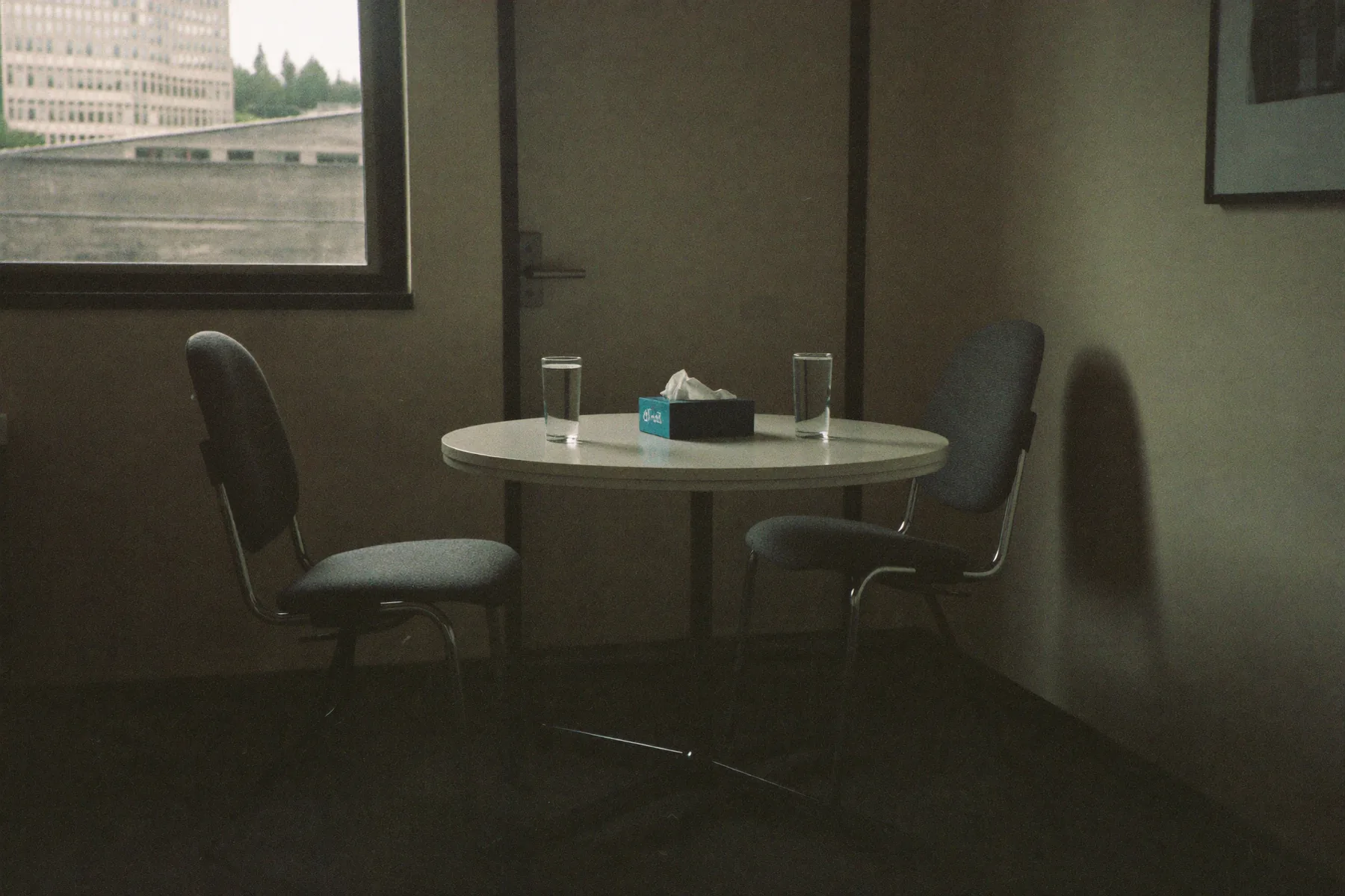 Twee stoelen aan een kleine ronde tafel in een rustige kamer, twee glazen water, niemand nog binnen