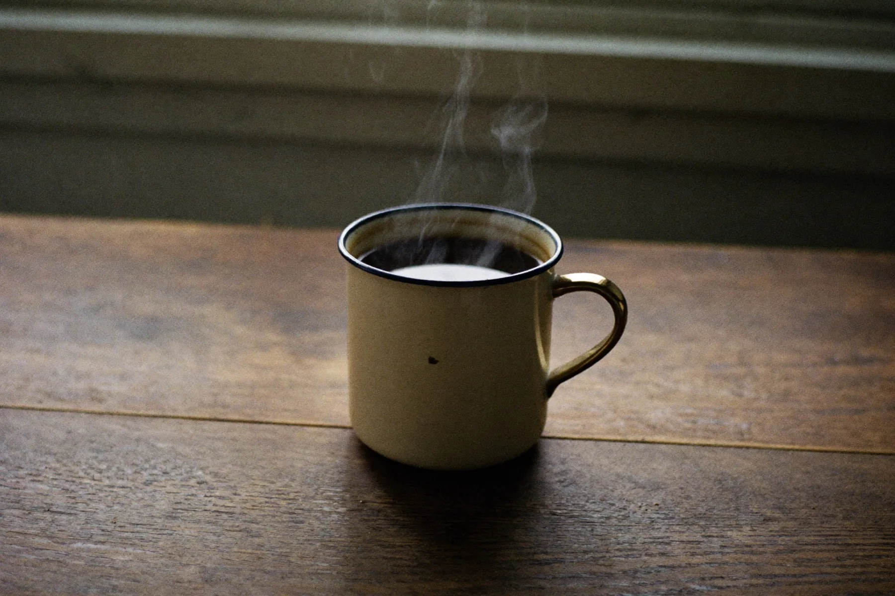 Een volle beker koffie op een houten tafel, ochtendzon erdoorheen.