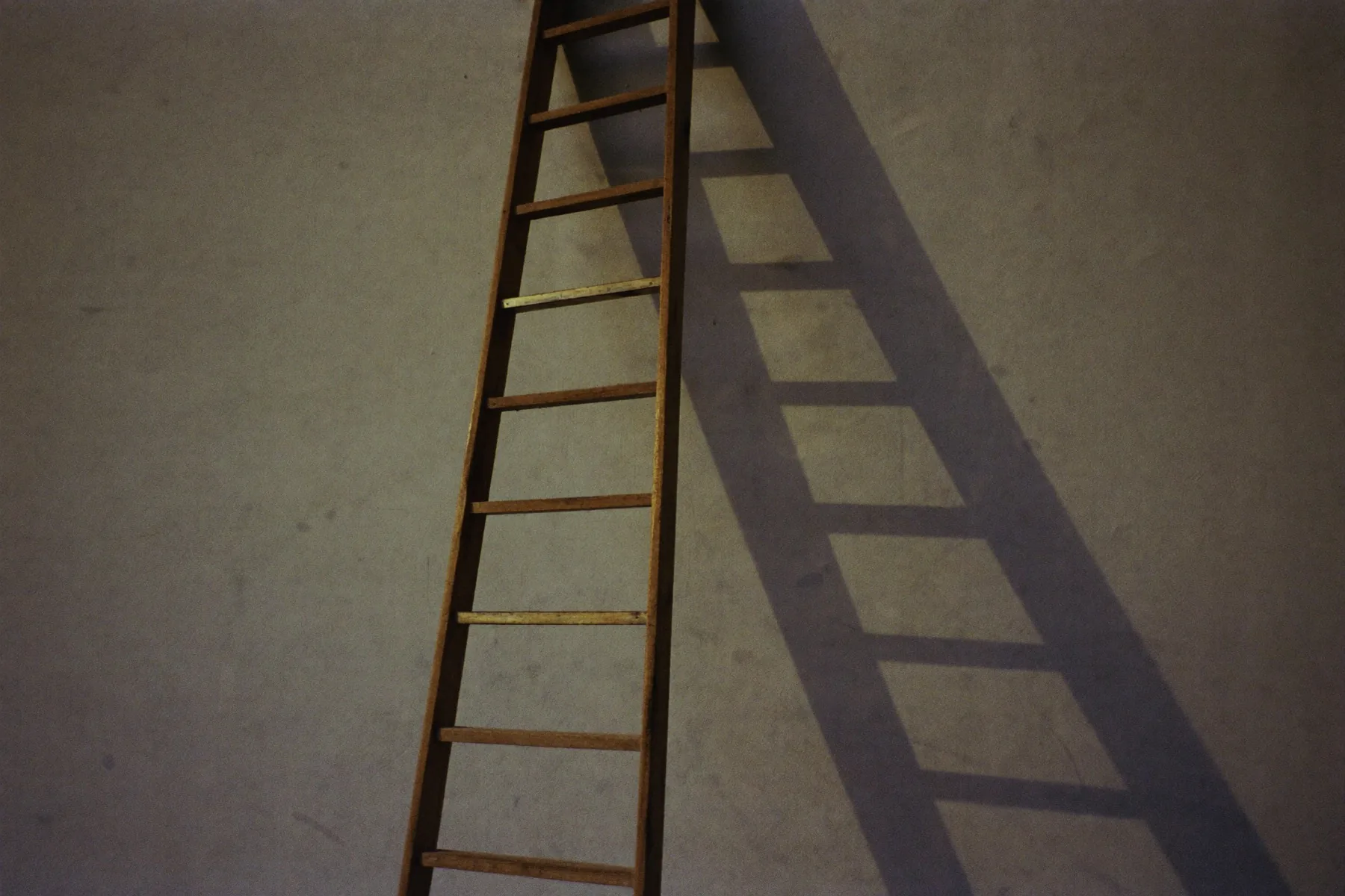 Een houten ladder die tegen een muur staat, lange schaduw in avondlicht.