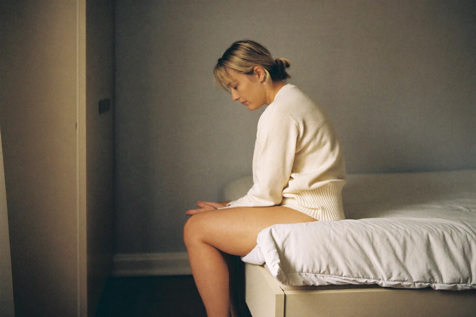 Een vrouw op de rand van haar bed in de ochtend, ellebogen op haar knieen